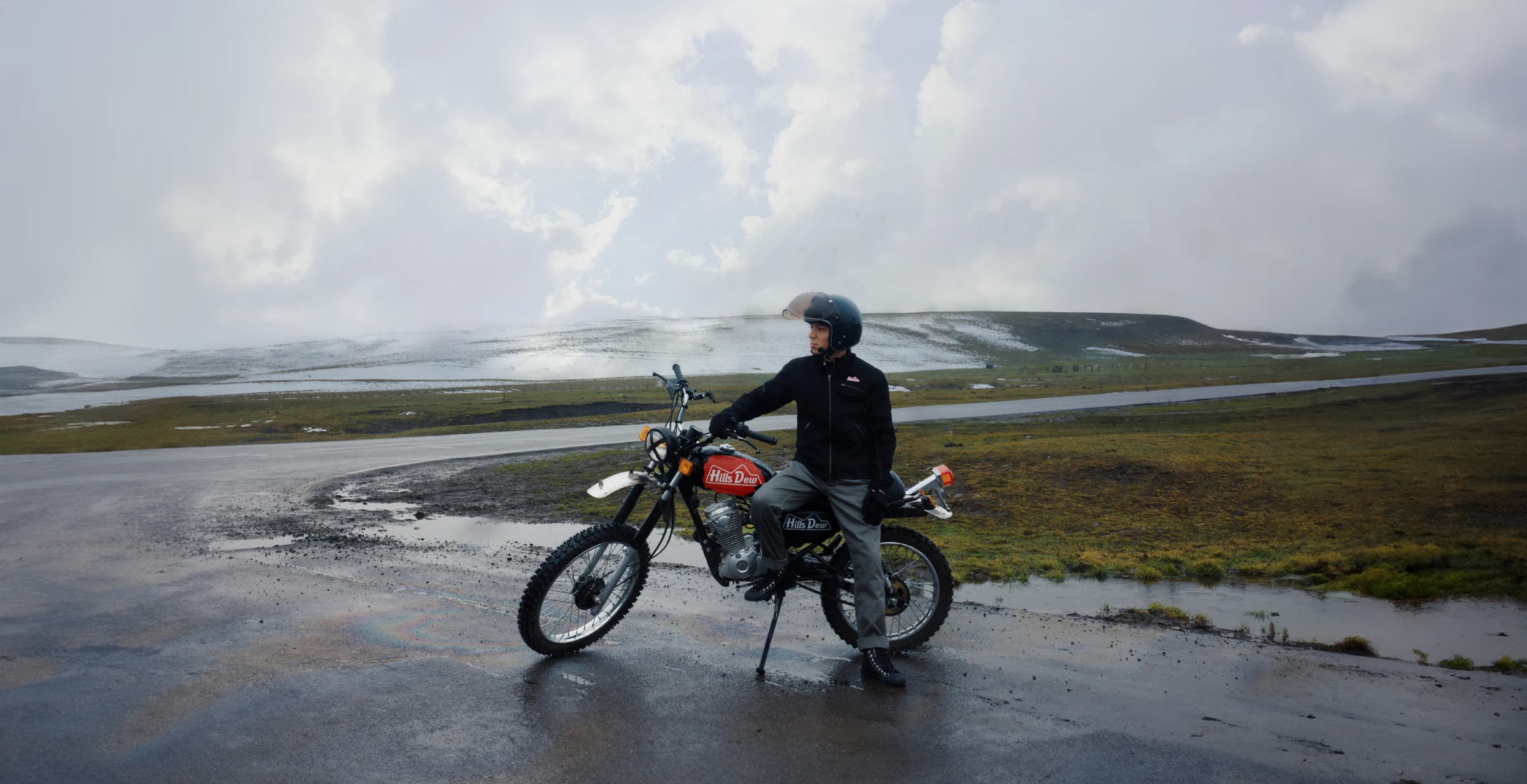 HillsDew jacket photographed beside a motorcycle on an open coastal road